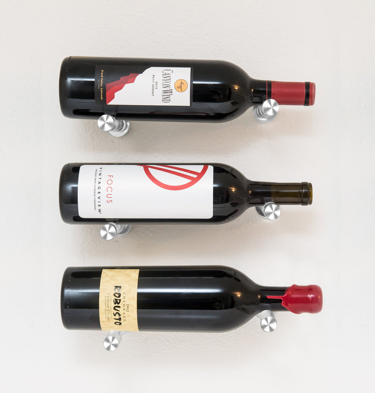 Wall wine bottle display with three bottles on round metal pins; black rack finish