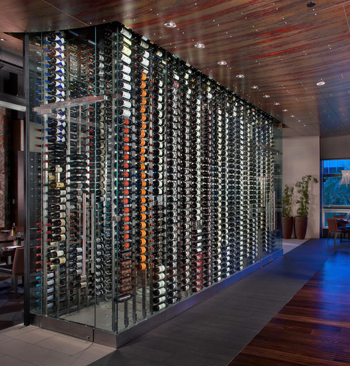 Double-sided wall wine rack with rows of filled wine bottles behind glass panels