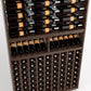 Wood wine rack with stacked black bottles on top rails and front corked bottle slots