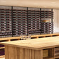 Wine bottle rack wall with horizontal shelves and bottles arranged above a wooden bar.