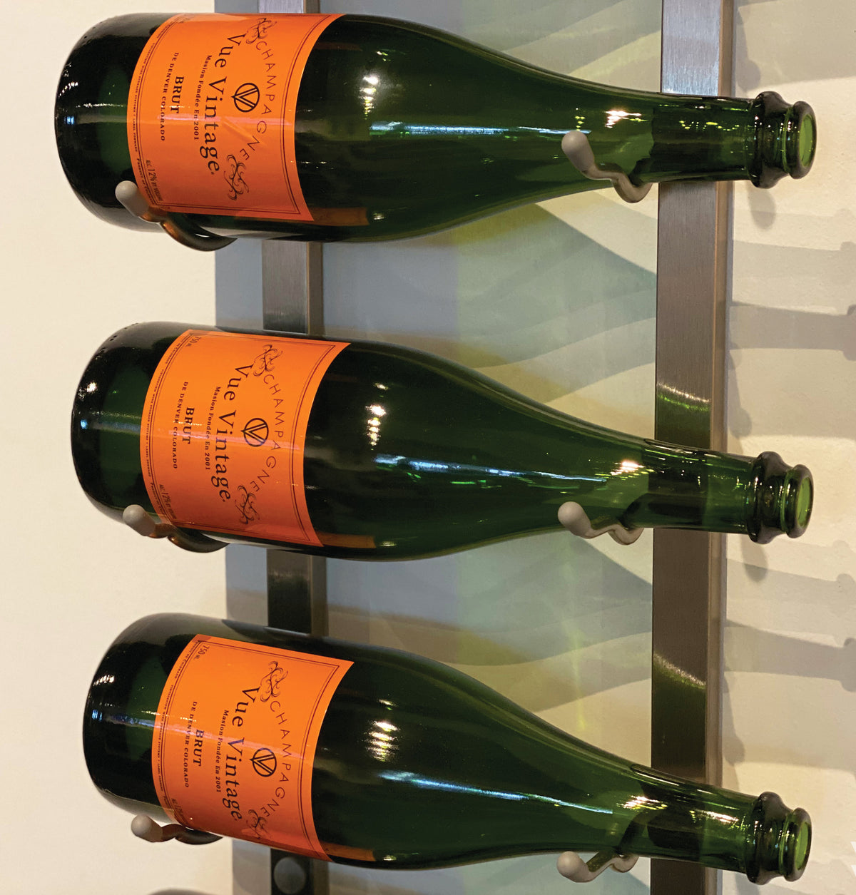 Wine bottle rack detail with green bottles and orange labels on vertical metal bars