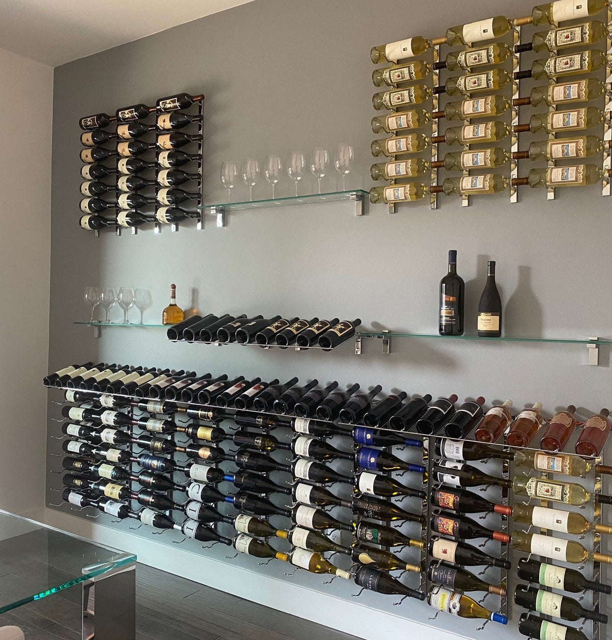 Wall-mounted wine bottle storage system with glass shelves and bottle racks