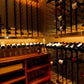 Wine bottle wall rack with rows of bottles in dark holders and countertop display