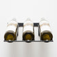 Wall-mounted wine bottle rack holding three bottles with white caps, front view.