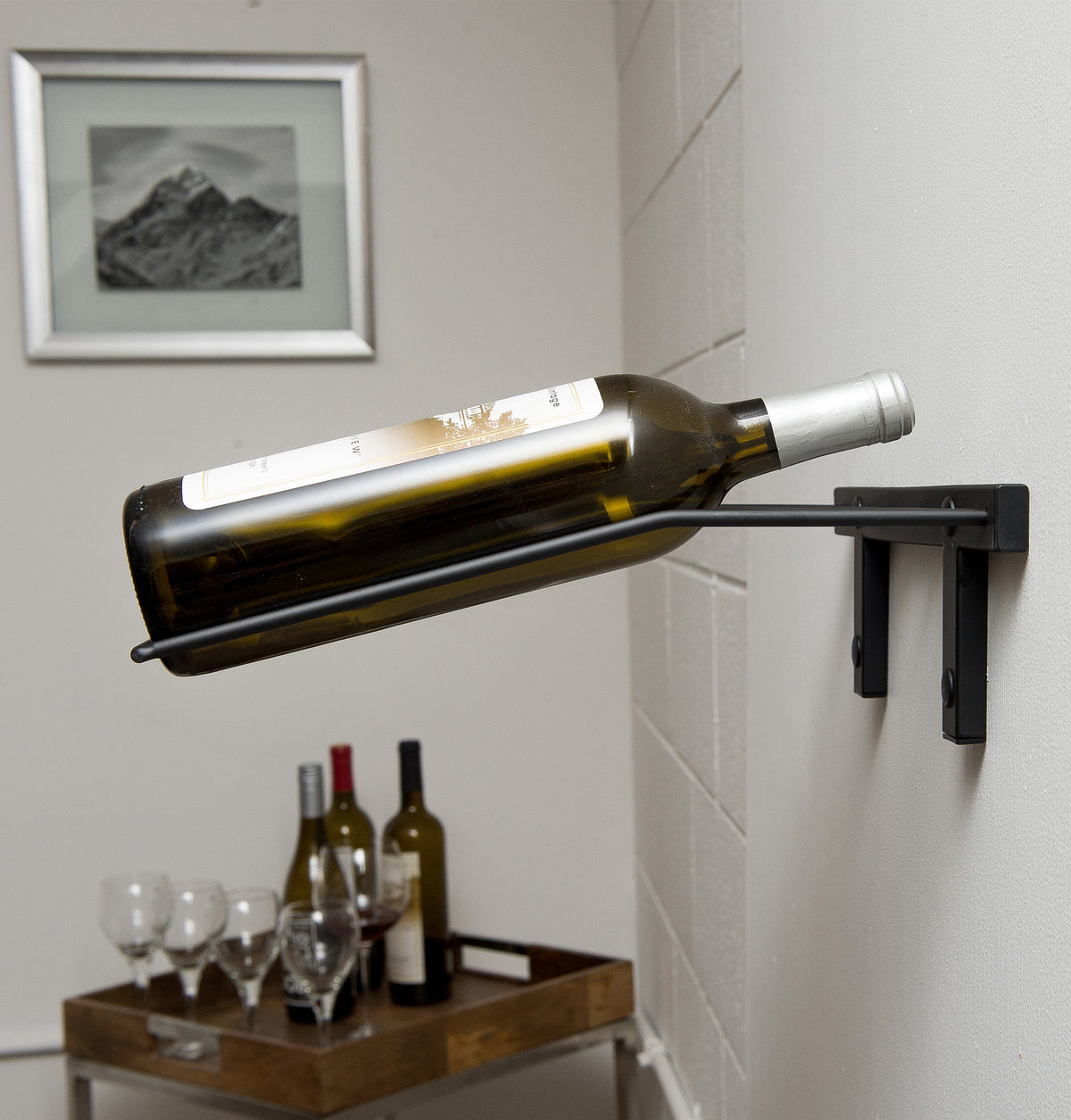 Wall-mounted wine bottle rack with one bottle held horizontally on a dark holder.