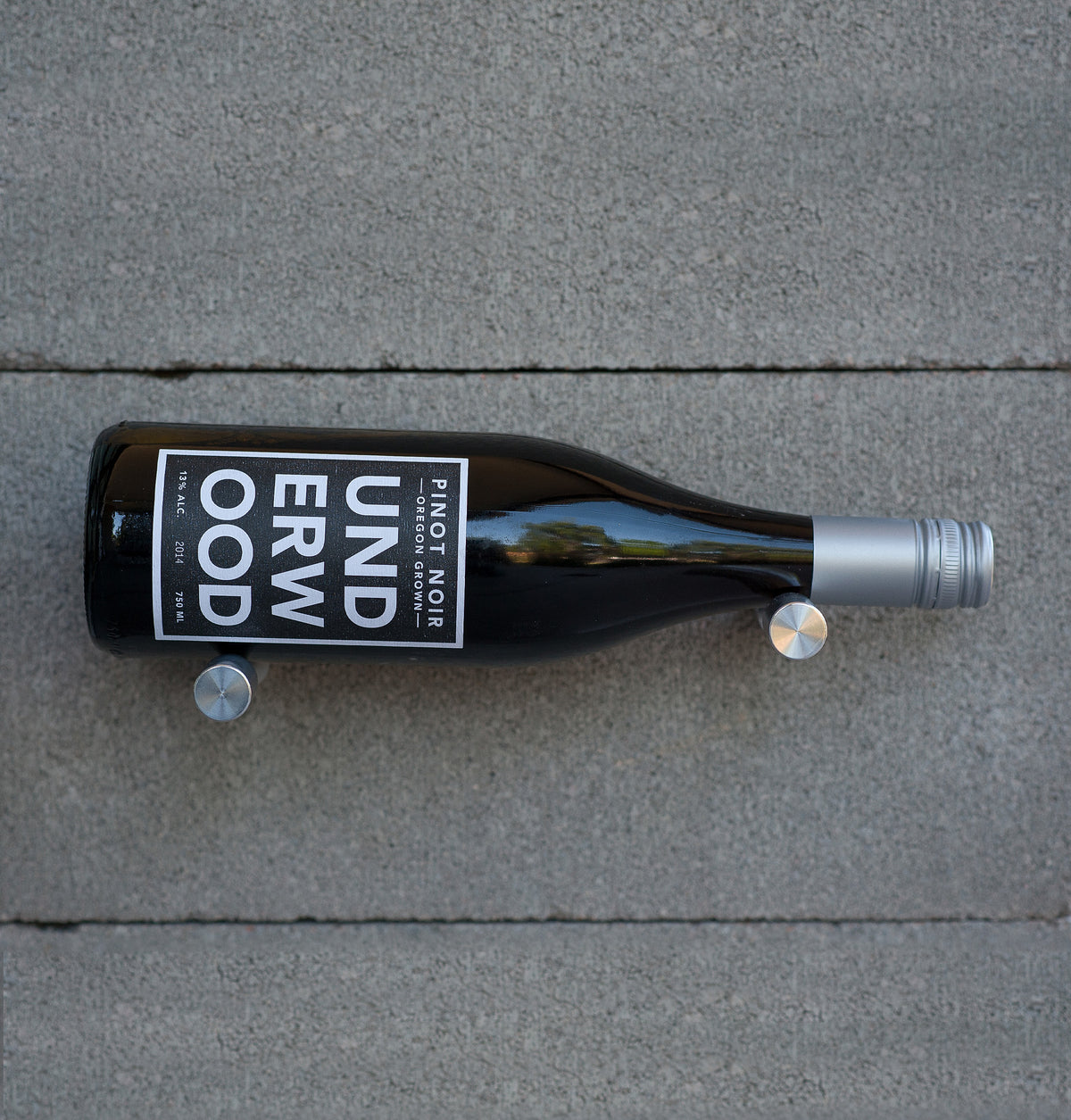Wine bottle holder pins with silver prongs securing a dark wine bottle on tile