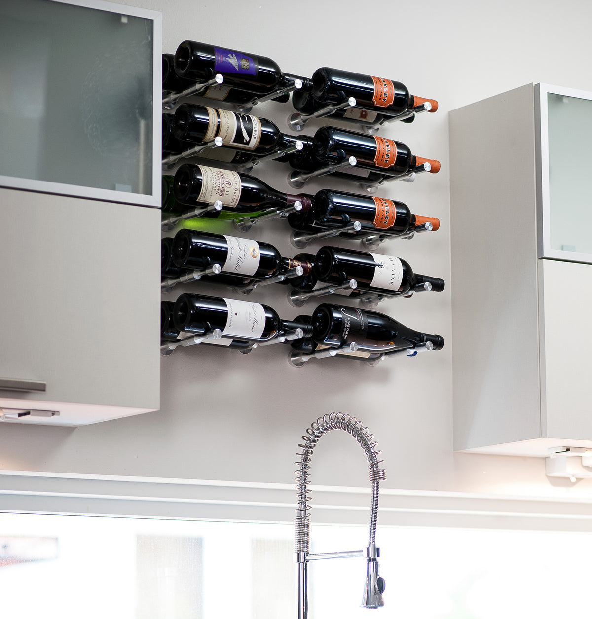 Wall-mounted wine bottle holder with curved metal pins beneath a cabinet rack