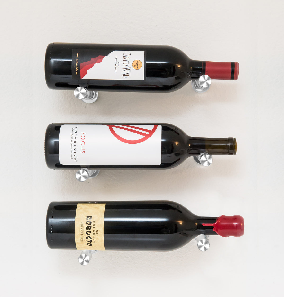 Wall wine bottle display with three bottles on round metal pins; black rack finish