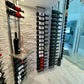 Wall-mounted metal wine shelf with bottle slots, dark frame and glass bottle displays