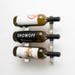 Wall-mount wine rack holding three wine bottles with black metal frame and curved pegs