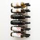 Wall wine rack with silver back plate holding six wine bottles on black pegs