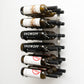 Wall wine rack with silver back plate holding six wine bottles on black pegs