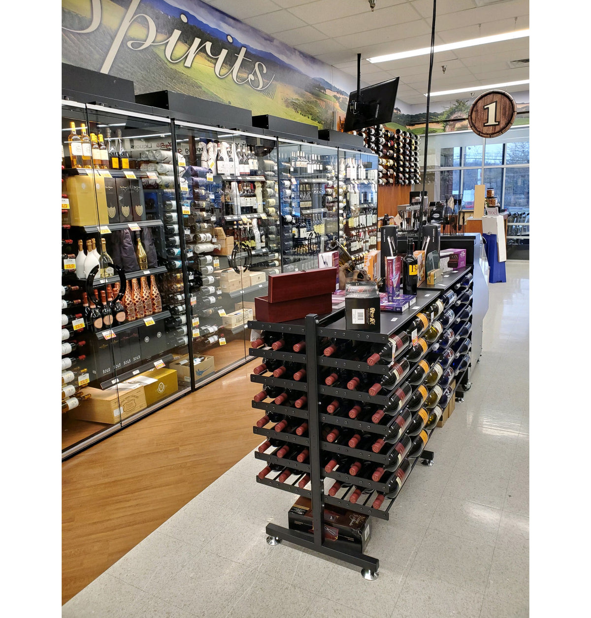 Double-sided wine bottle display rack with shelf, black metal, in retail store on casters