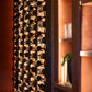 Wall-mounted wine bottle rack with black frame and cork-style pegs, filled with bottles