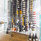 Wall-mounted wine bottle display with many bottles arranged on peg rails behind glass panels.