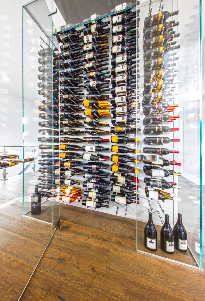 Wall-mounted wine bottle display with many bottles arranged on peg rails behind glass panels.