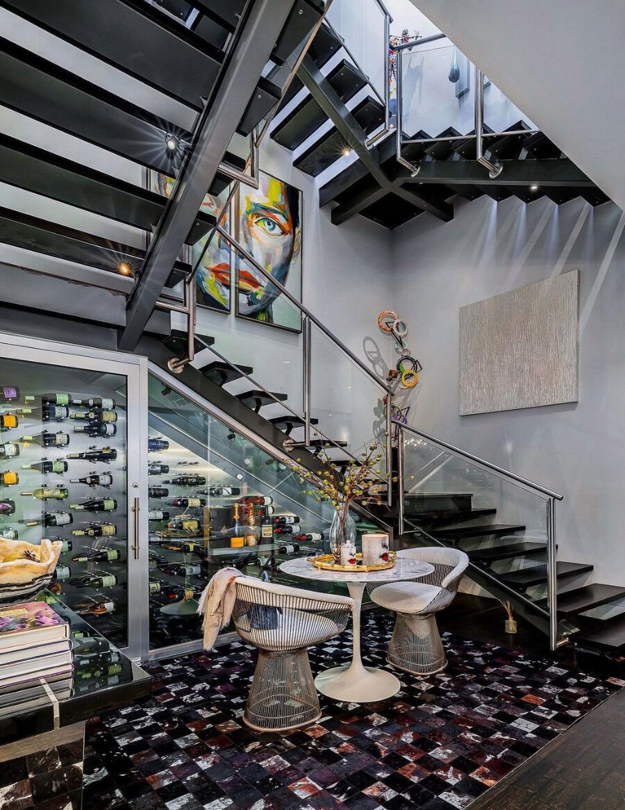 Aluminum wine bottle display wall with bottles next to a stairwell and dining area