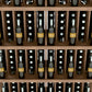 Wood wine bottle wall display with five shelves holding wine bottles in slots