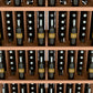 Natural wood wine bottle wall display with five shelves and rows of bottle slots