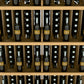 Wine bottle display shelf close-up with light wood slats and filled bottle openings