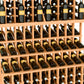 Light wood triple-tier wine bottle display rack with double-deep base, filled with bottles