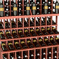 Triple-tier wine bottle display rack with double-deep base; reddish-brown wood frame, bottle rows